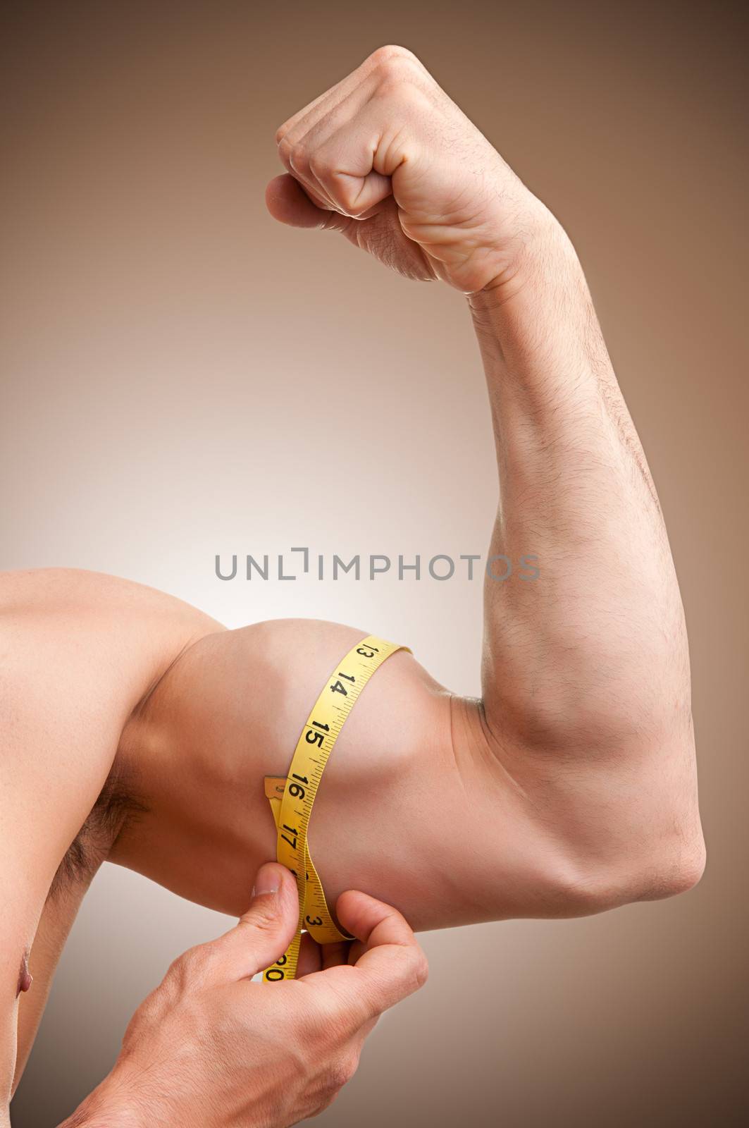 Fit man measures his bicep with a yellow tape