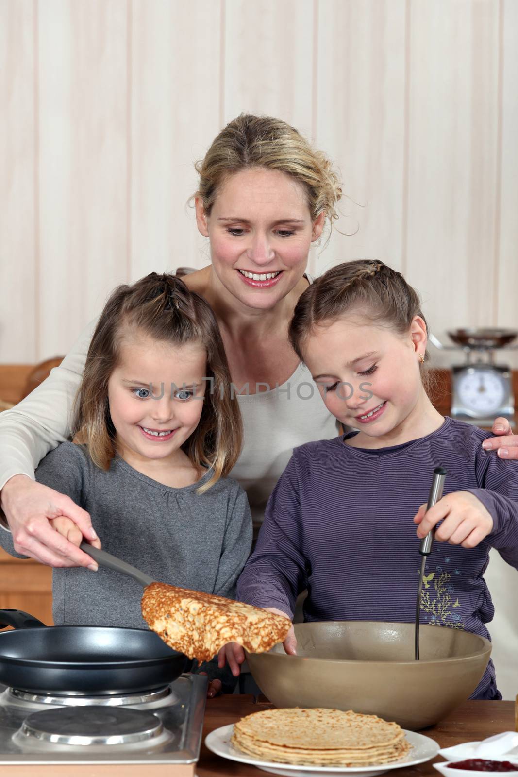 Mother and daughters cooking pancakes by phovoir