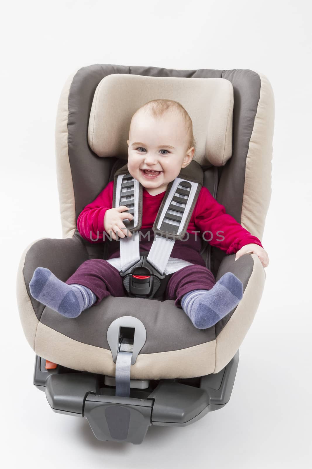 laughing child in booster seat for a car in light background.