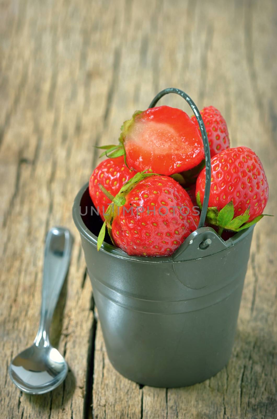 Fresh strawberries in bucket isolated on wooden background