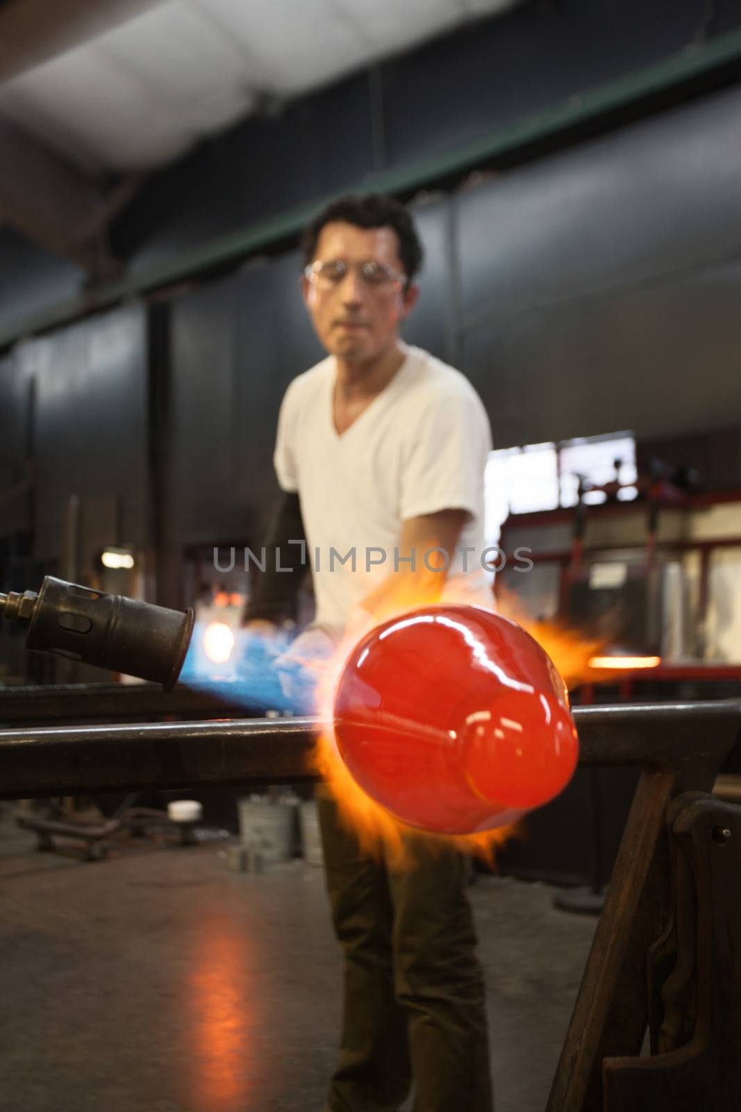 Glass factory worker forming glass object on flame