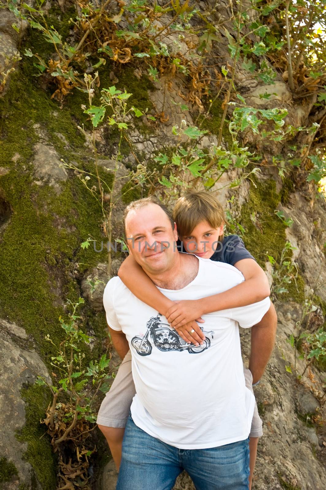 Man giving young boy piggyback ride outdoors smiling .