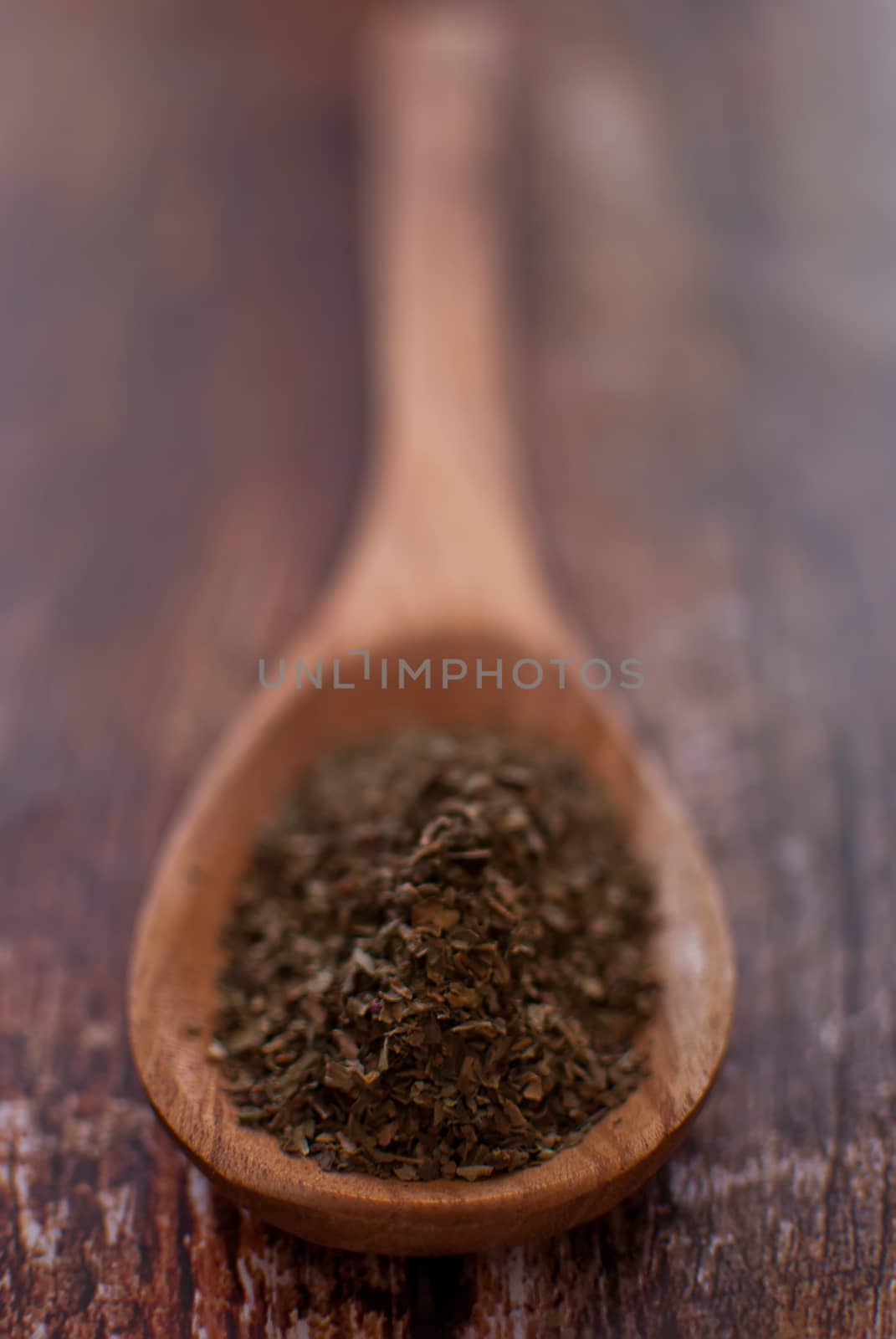 basil spice in wooden spoon over wood background - selective focus