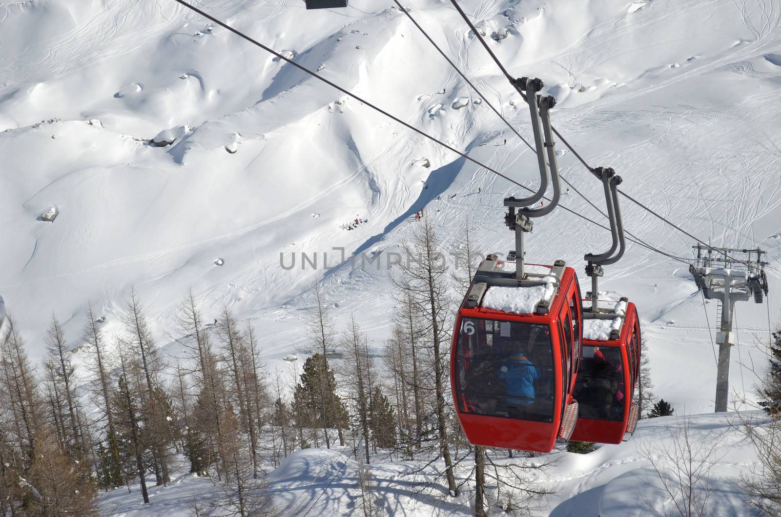 Two red cablecars climbing snow covered mountain, seen from above