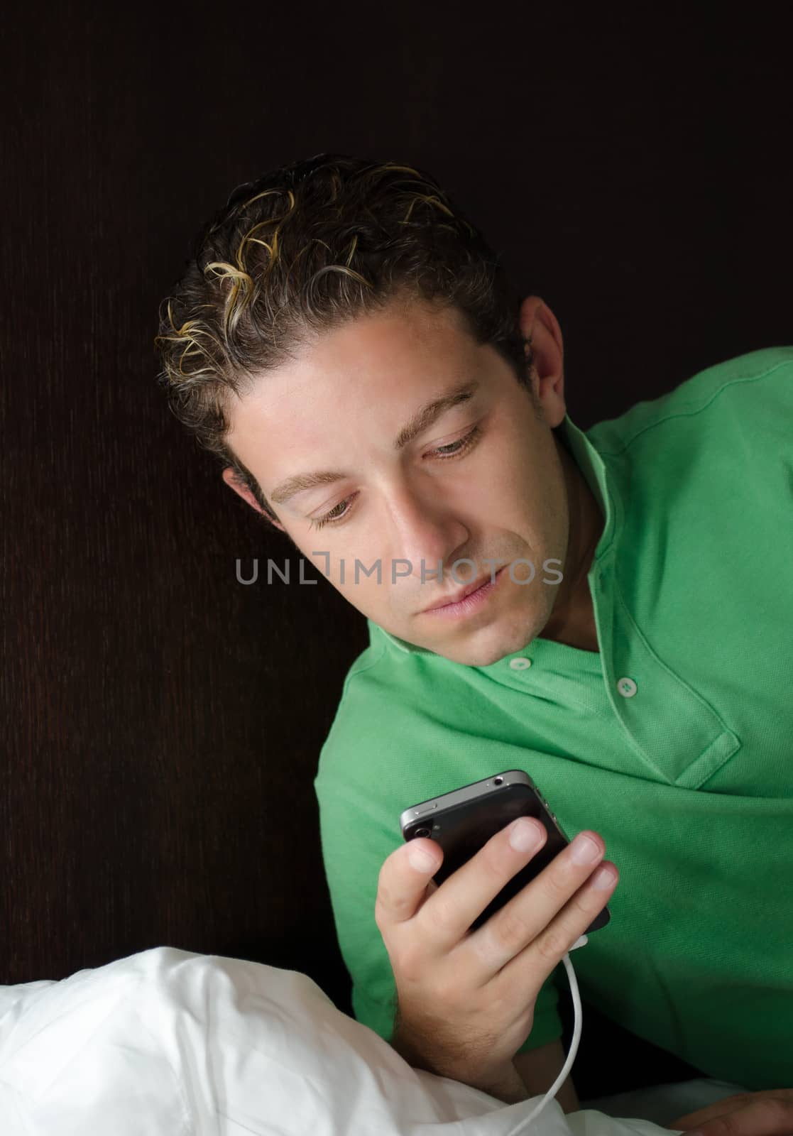 Handsome young man looking at or reading cell phone screen at night in bed