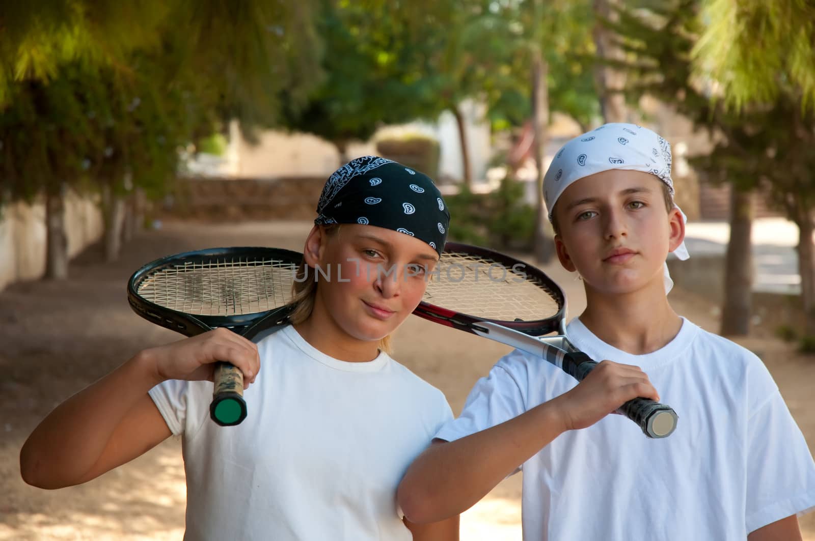 Two young male friends with rackets on tennis court smiling .