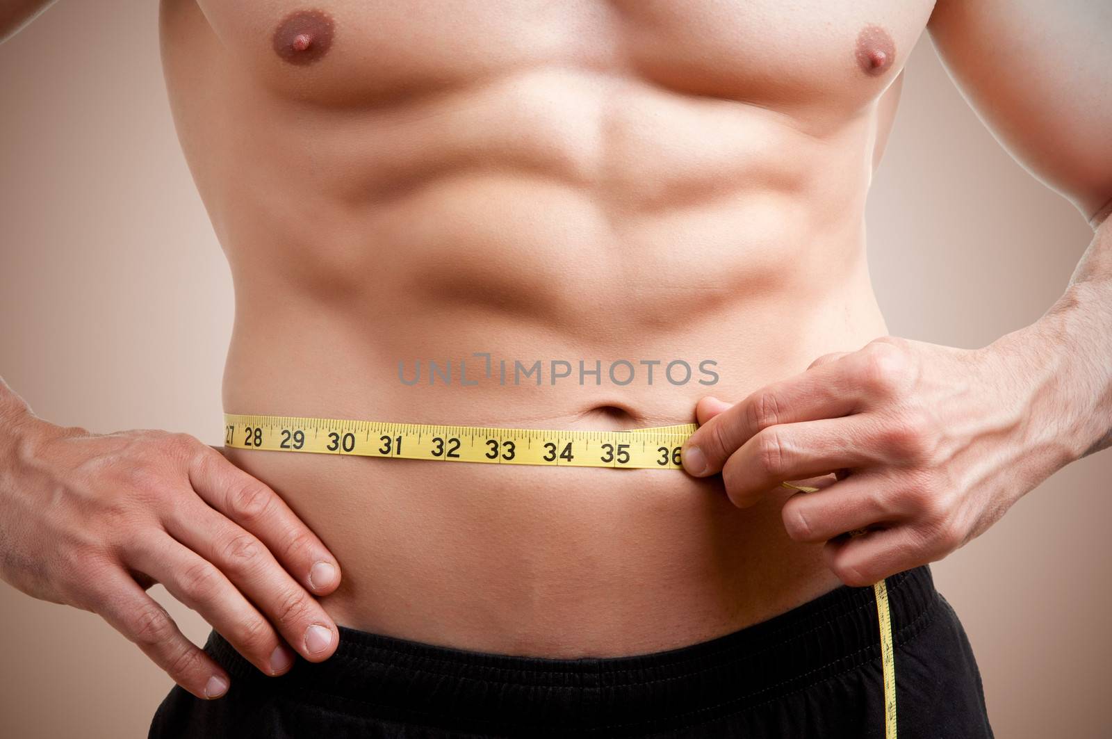 Fit man measuring his waist after a workout in the gym