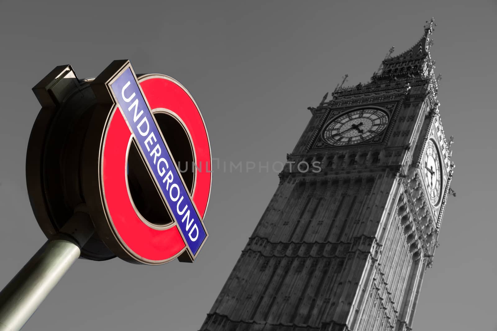 A black a white image of the palace of Westminster with a color image of the underground sign in the foreground