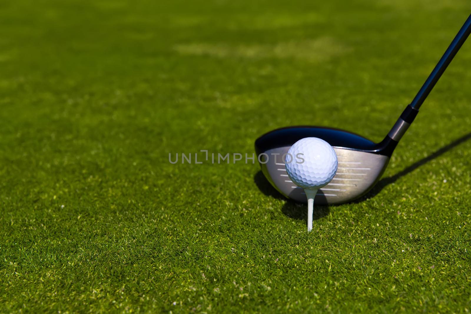 Close up of a golf ball on a tee with a club behind waiting to hit it.