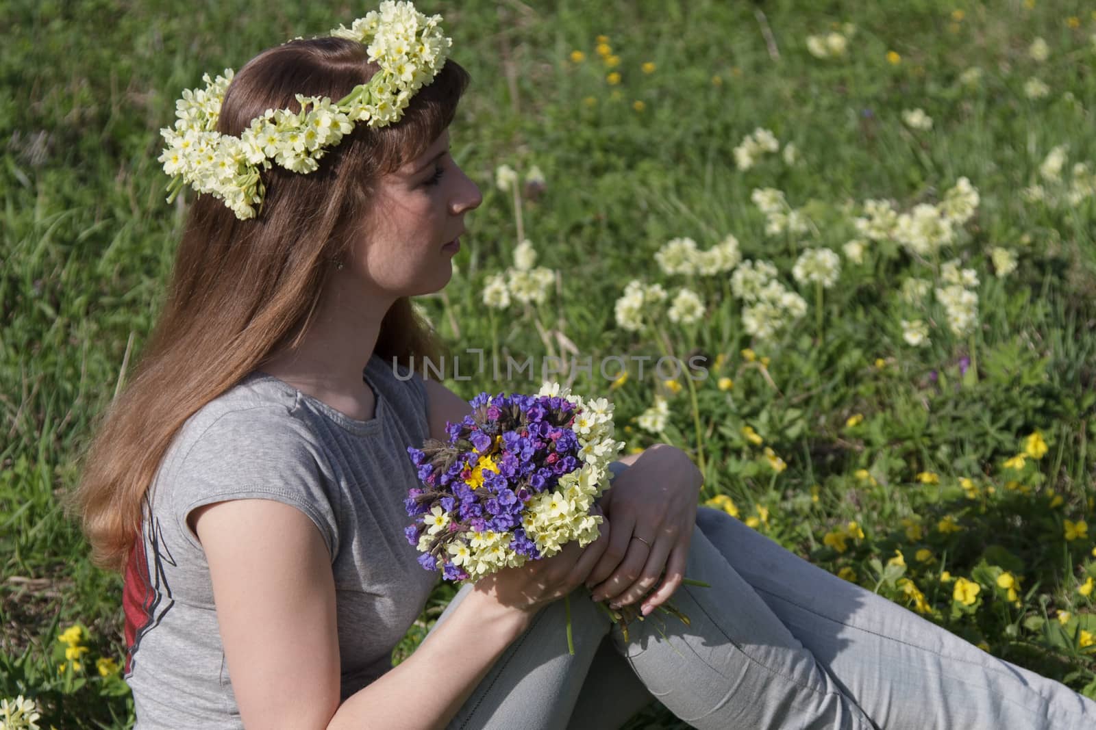 Girl with a wreath and a bouquet of spring on the lawn