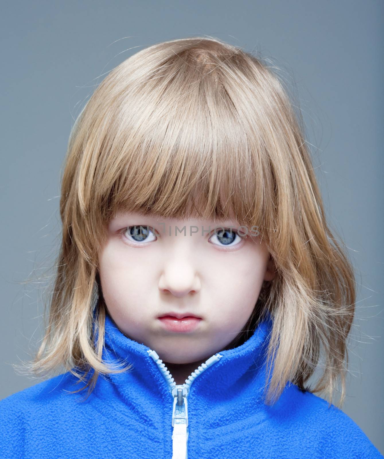 portrait of a boy with long blond hair in blue top - isolated on gray