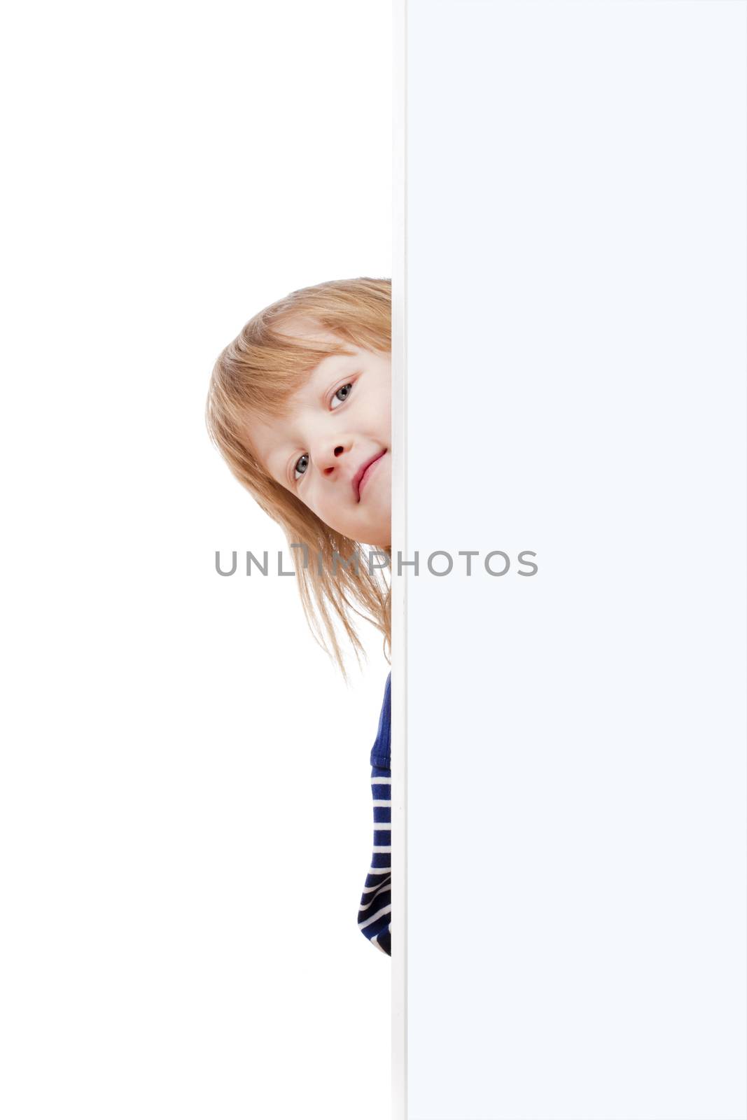 curious boy with long blond hair peeking out from behind a white board looking