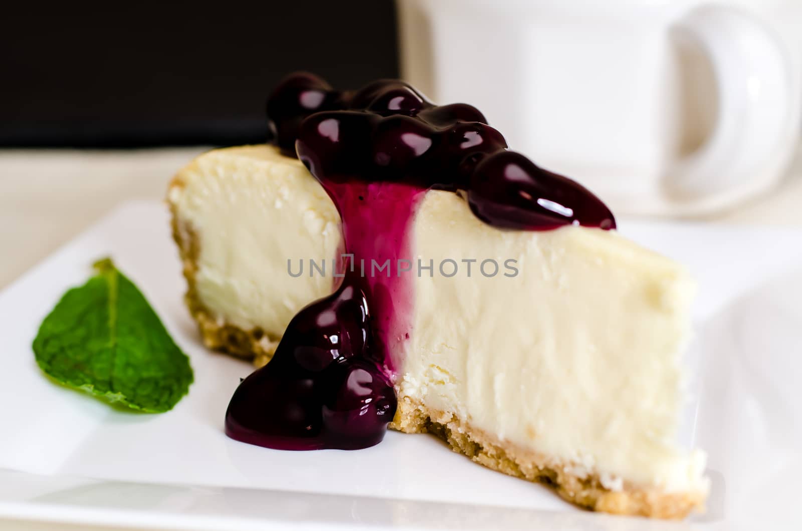 Slice of blueberry cheesecake and coffee with mint garnish.  Shallow depth of field.
