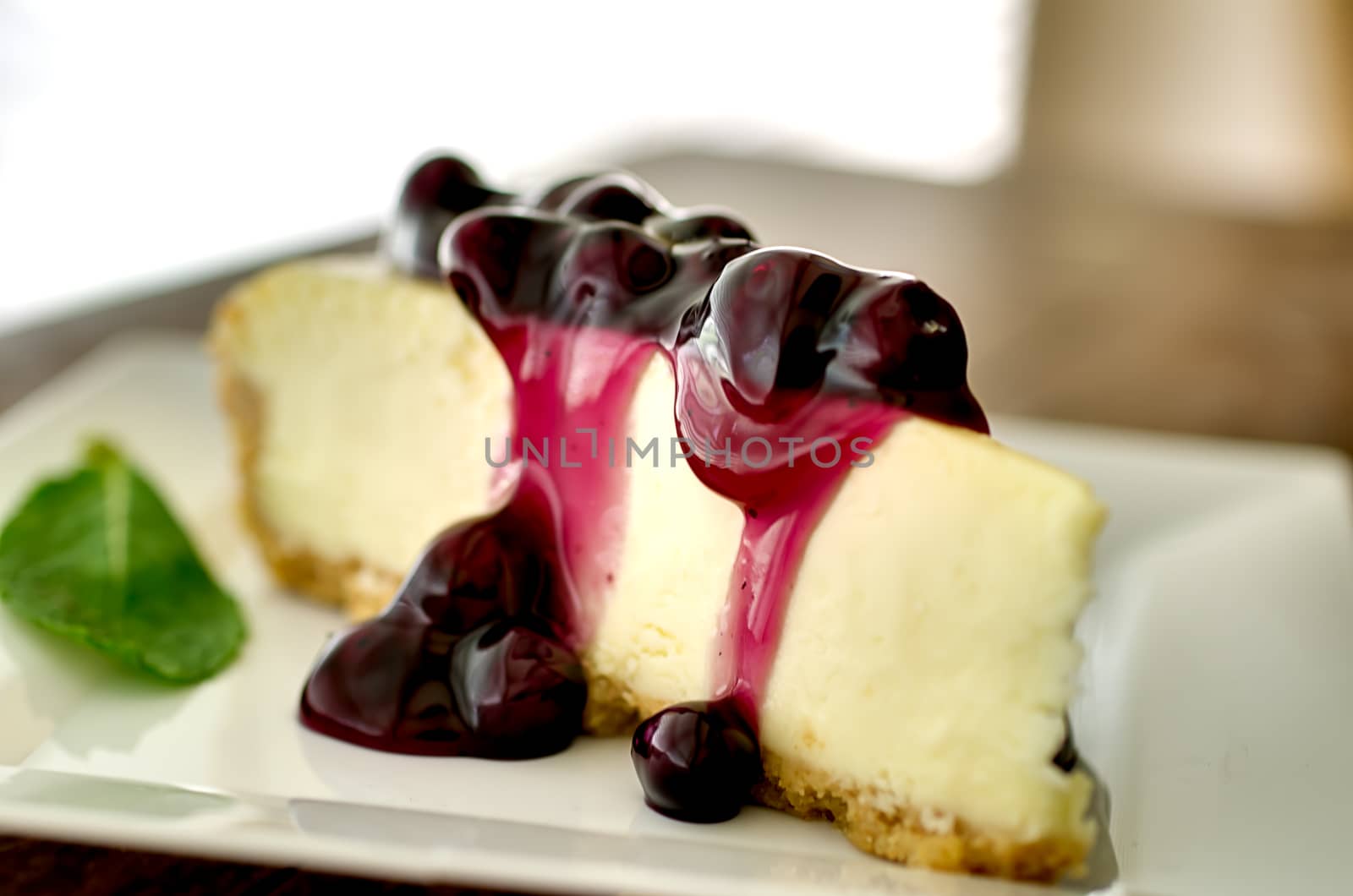 Slice of blueberry cheesecake in the afternoon with mint garnish.  Shallow depth of field.