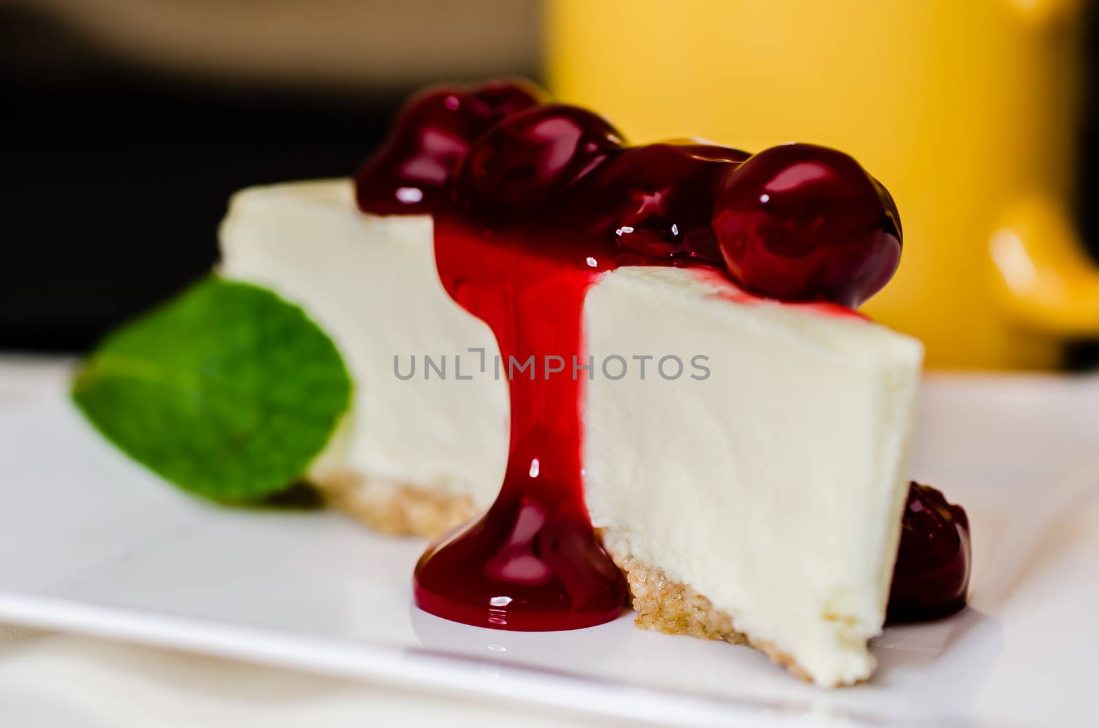 Slice of cherry cheesecake and coffee with mint garnish.   Shallow depth of field.  