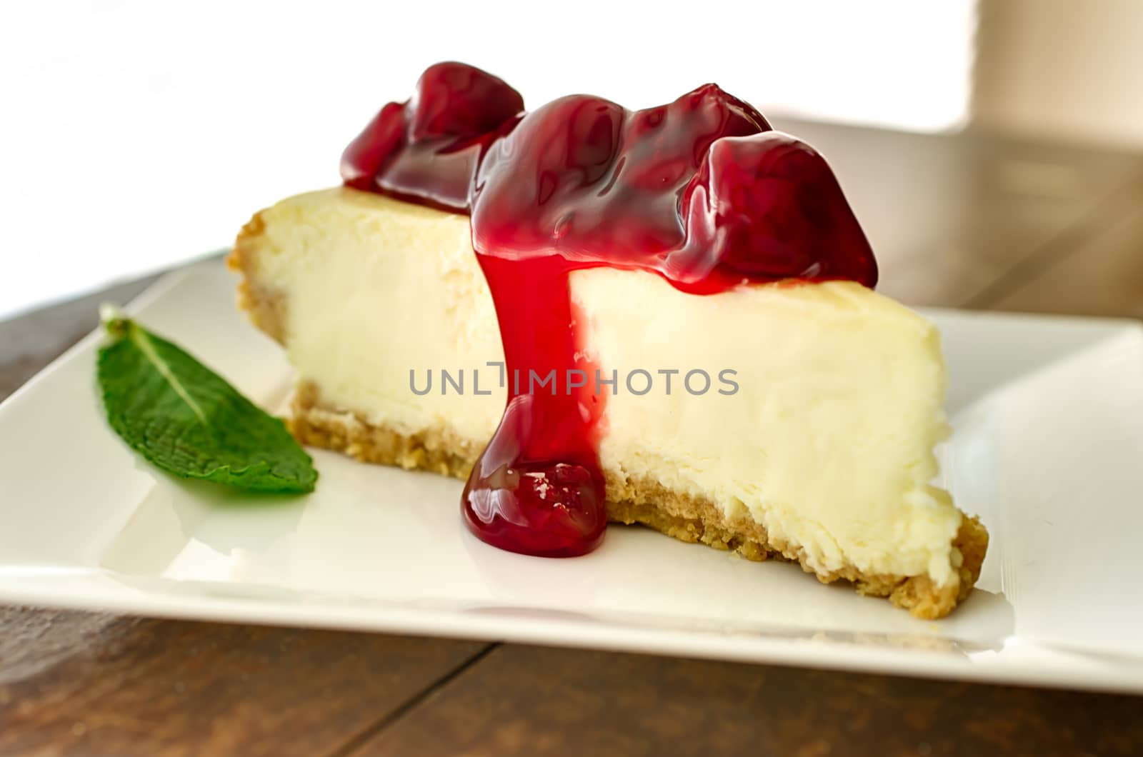 Slice of cherry cheesecake in the afternoon with mint garnish.   Shallow depth of field.  