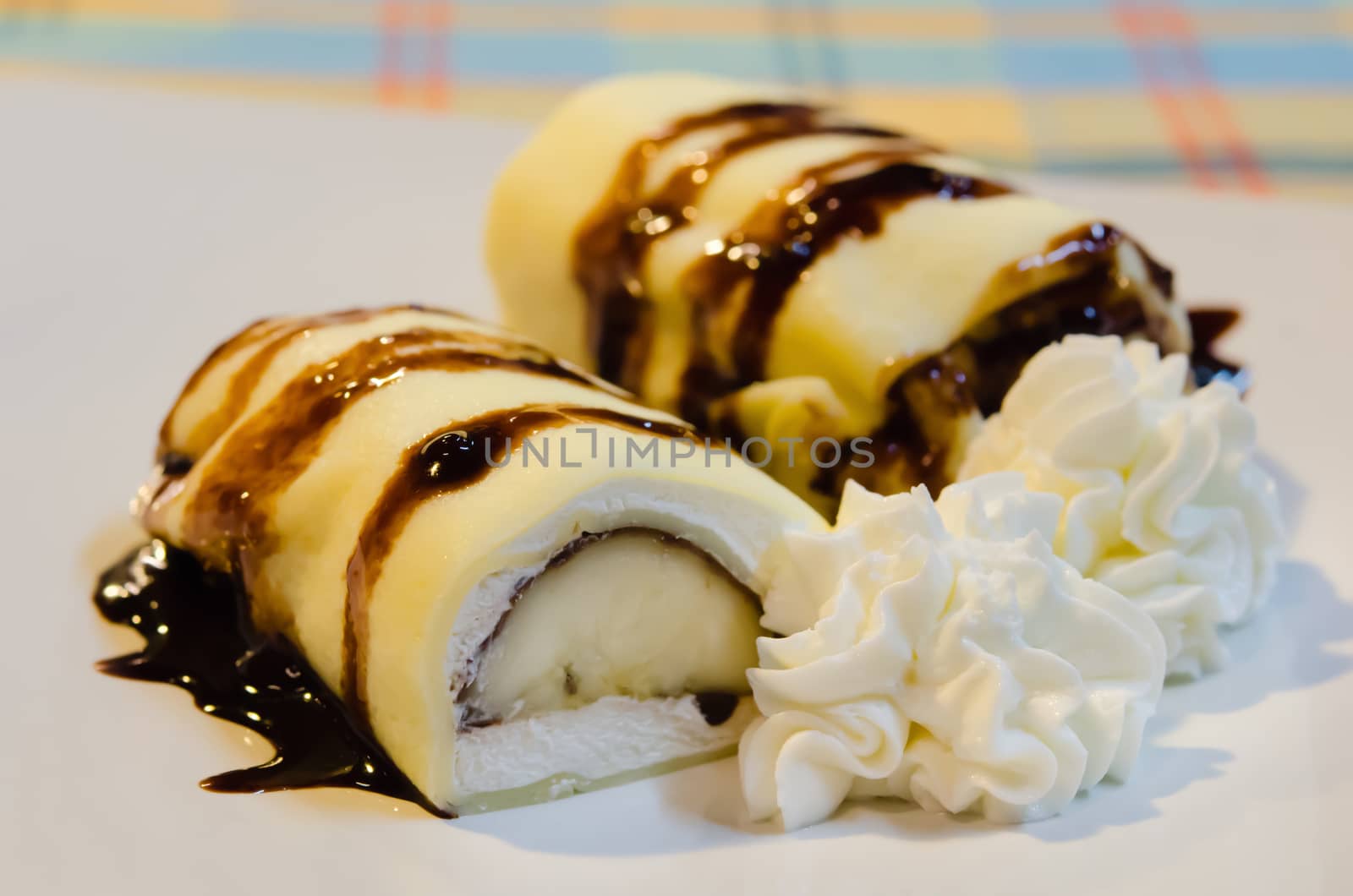 banana crepe rolls filled  with white cream and banana,   topping with chocolate  syrup served with whipping cream