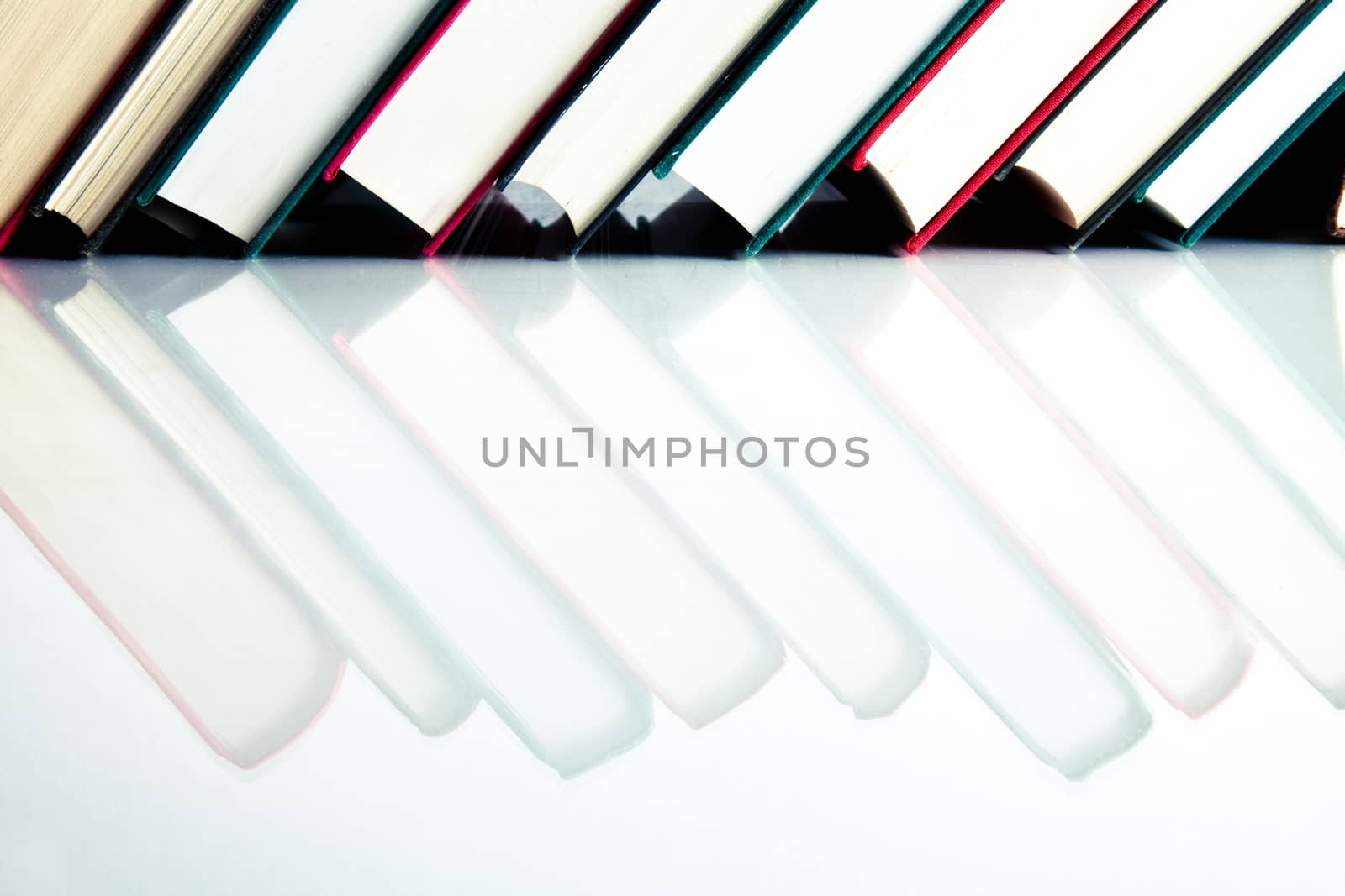 Red, black and green books in a row on white reflective surface