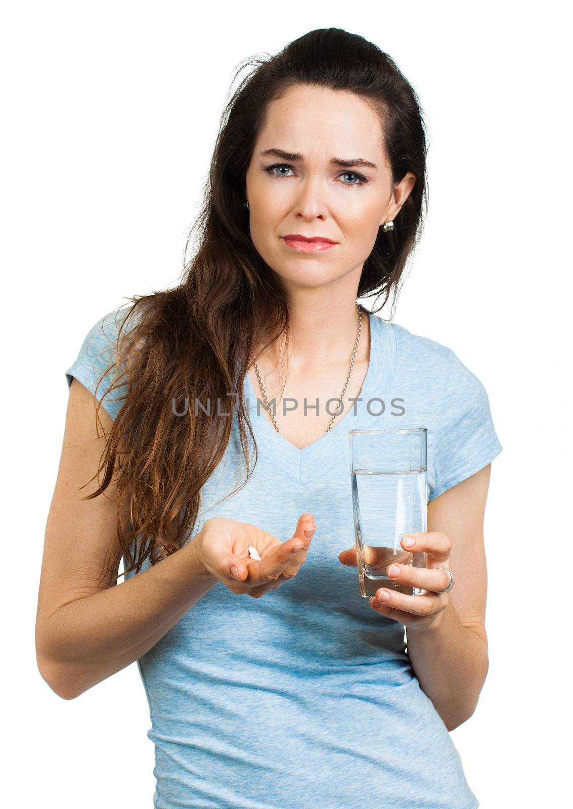 An unhappy woman in pain holding glass of water and pain killer pill, looking at camera. Isolated on white.
