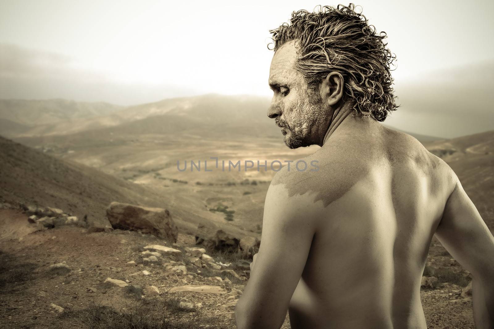 Warrior man covered in mud on desert background