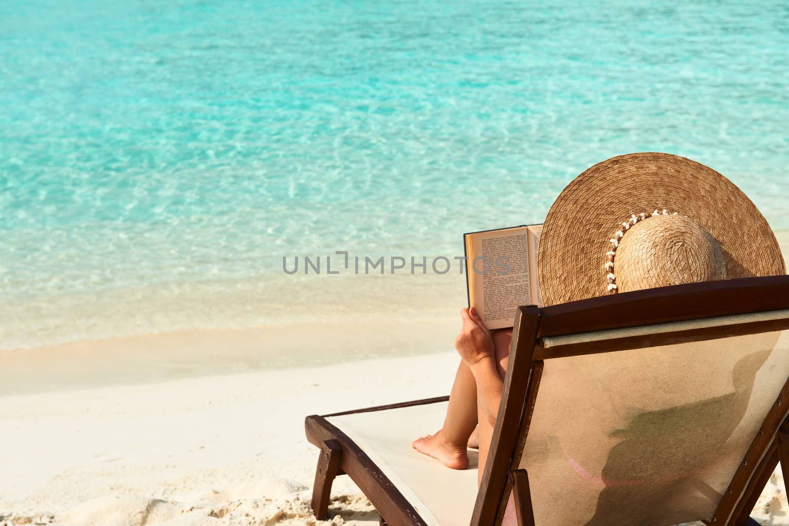Young woman reading a book at beach by haveseen