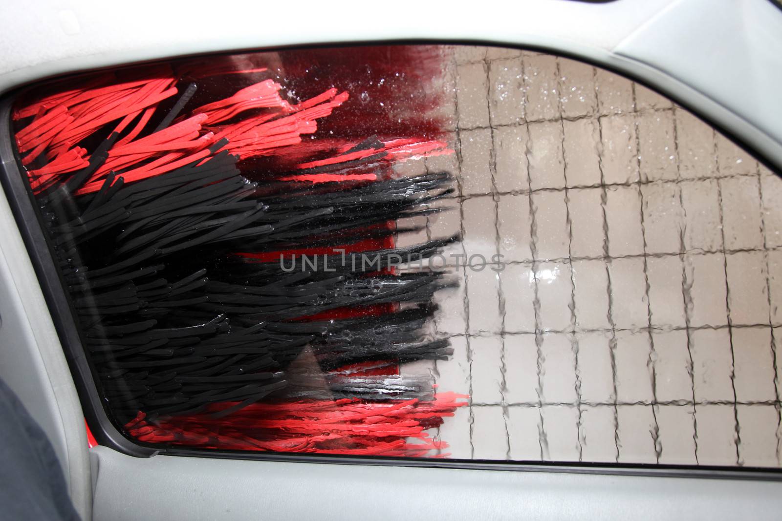 View through the side window from inside a car in a car wash with the rollers rotating on the bodywork