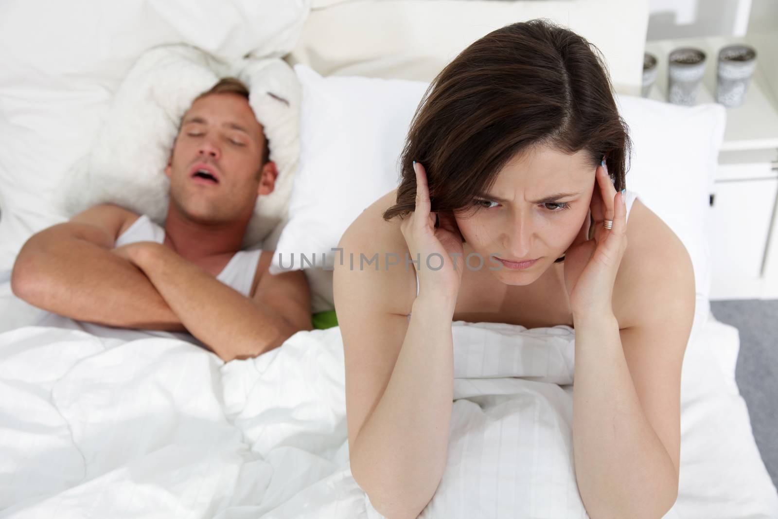 Marital problems in the bed with a woman suffering from insomnia trying to block her ears against her husbands loud snores