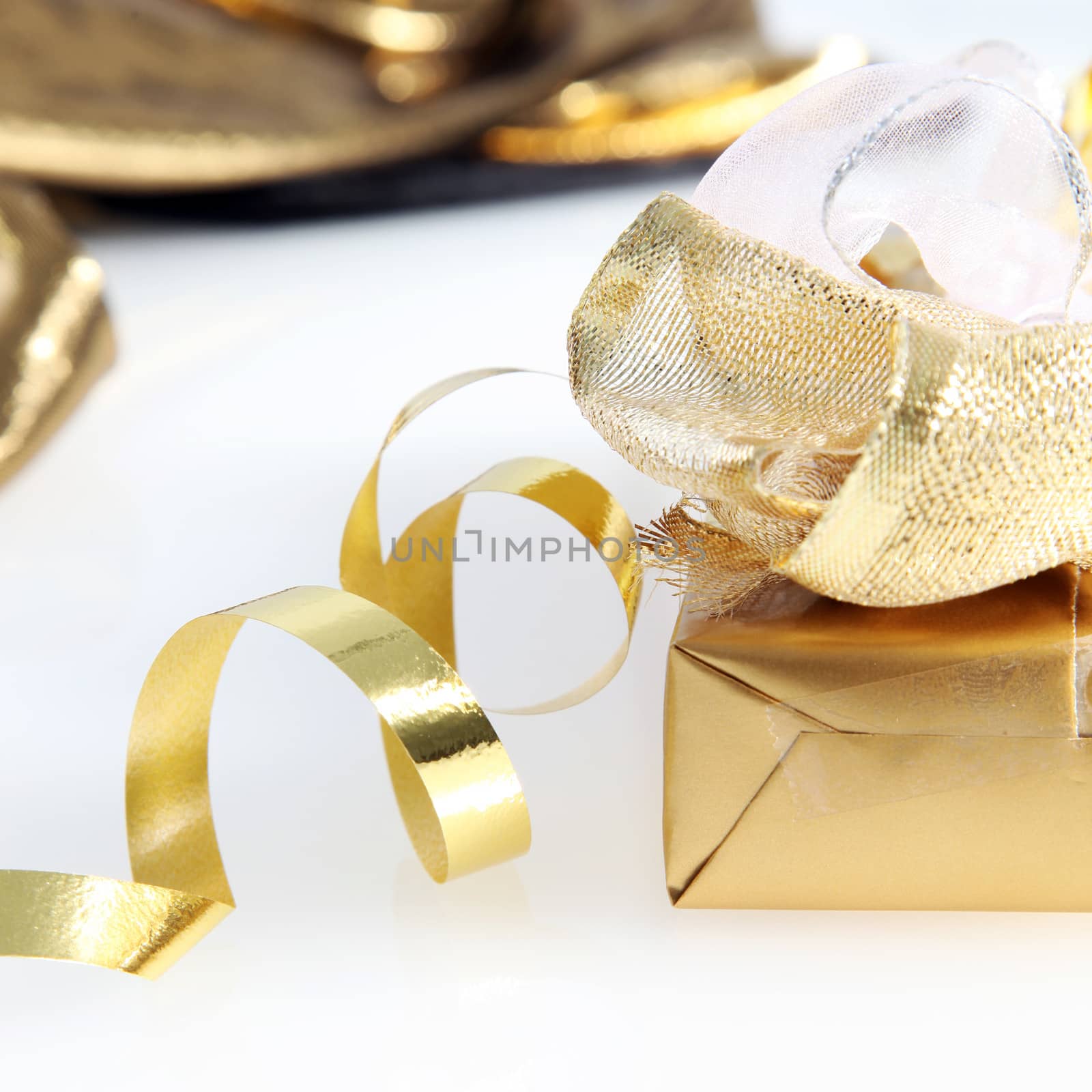 Closeup of a pretty gold wrapped gift and twirled ribbon on a white background for your seasonal greeting