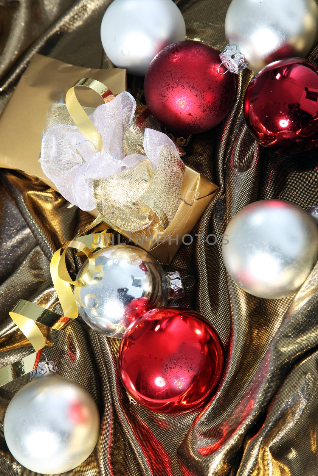 Shiny red and silver Christmas baubles nestling in luxurious gold fabric with a decorative gold wrapped gift box