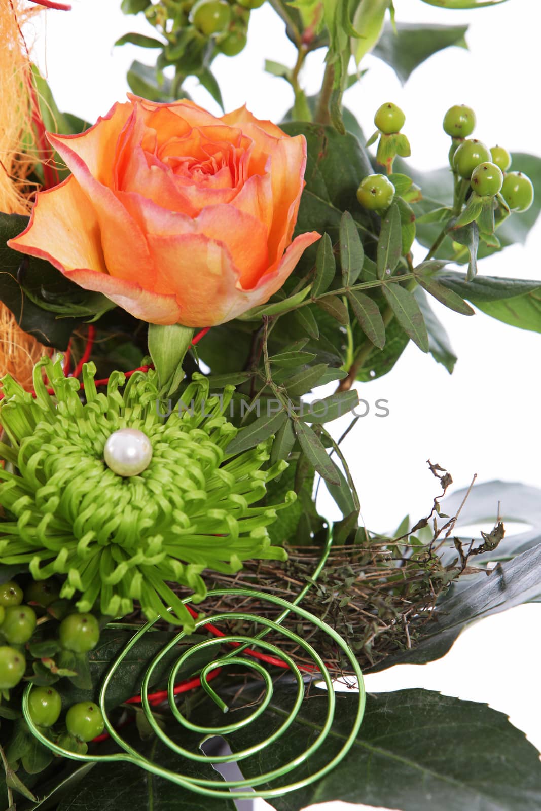 Flowers in a creative wedding display with spiral wires and a pearl on greenery with an orange rose