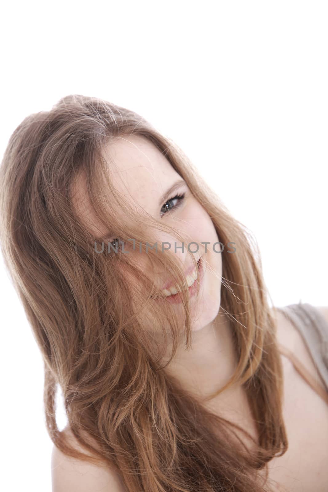 Cute teenage girl smiling at the camera through her hair which is falling over her face, isolated on white