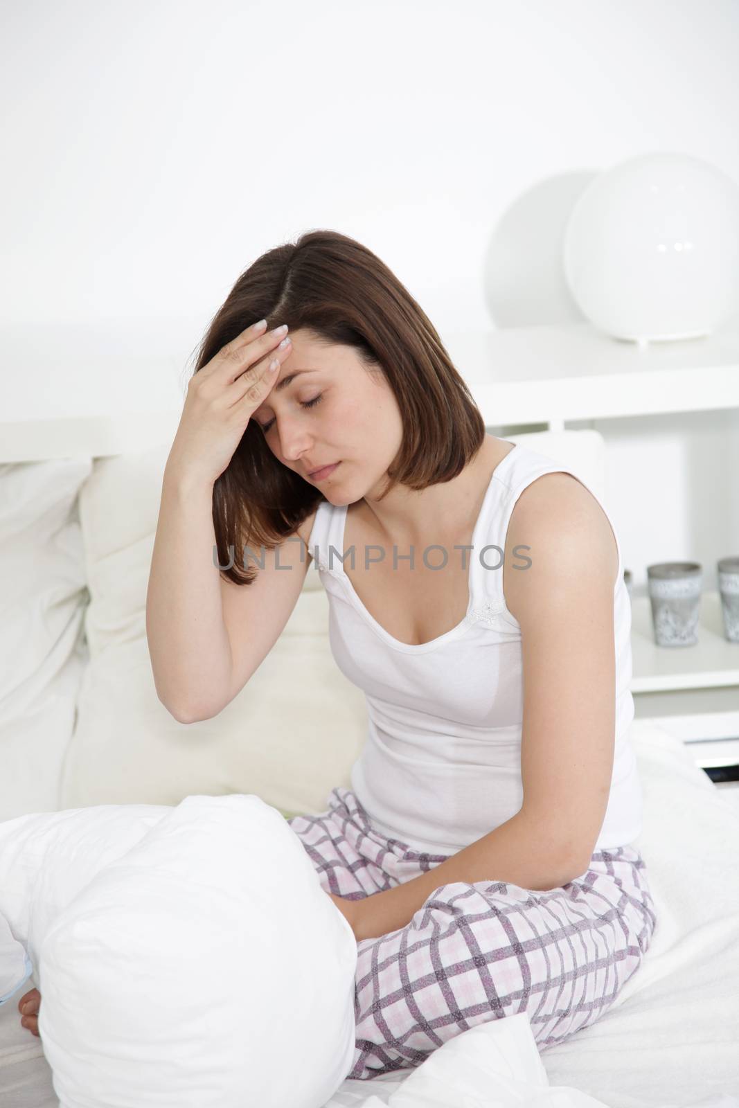 Tired woman with a headache sitting on the edge of her bed in her nightwear holding her head with her hand
