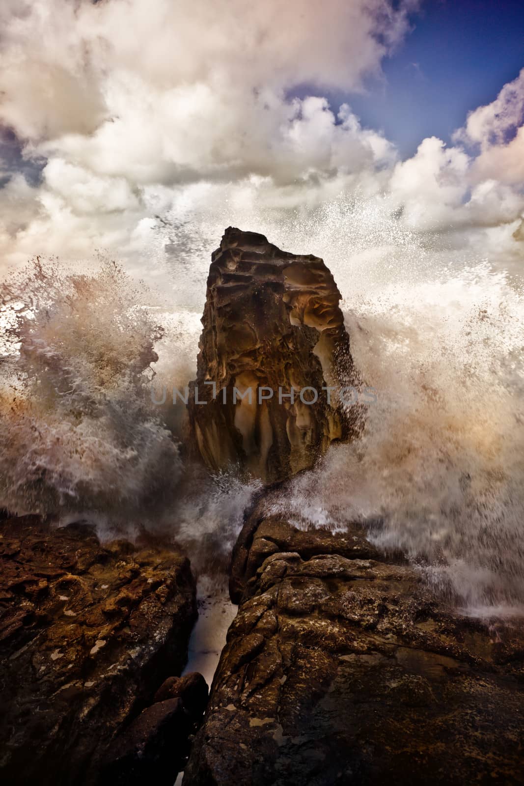 Waves breaking on a rock against a dramatic sky by jrstock