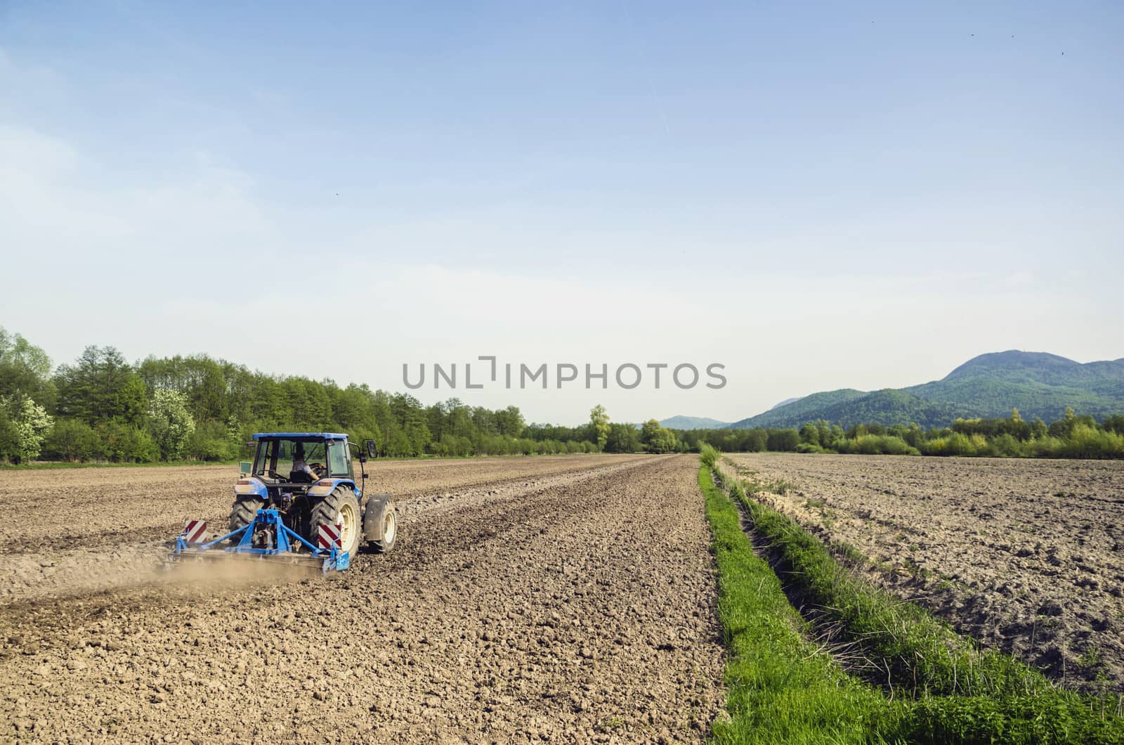 Farmer in blue tractor plowing field surrounded by forests.