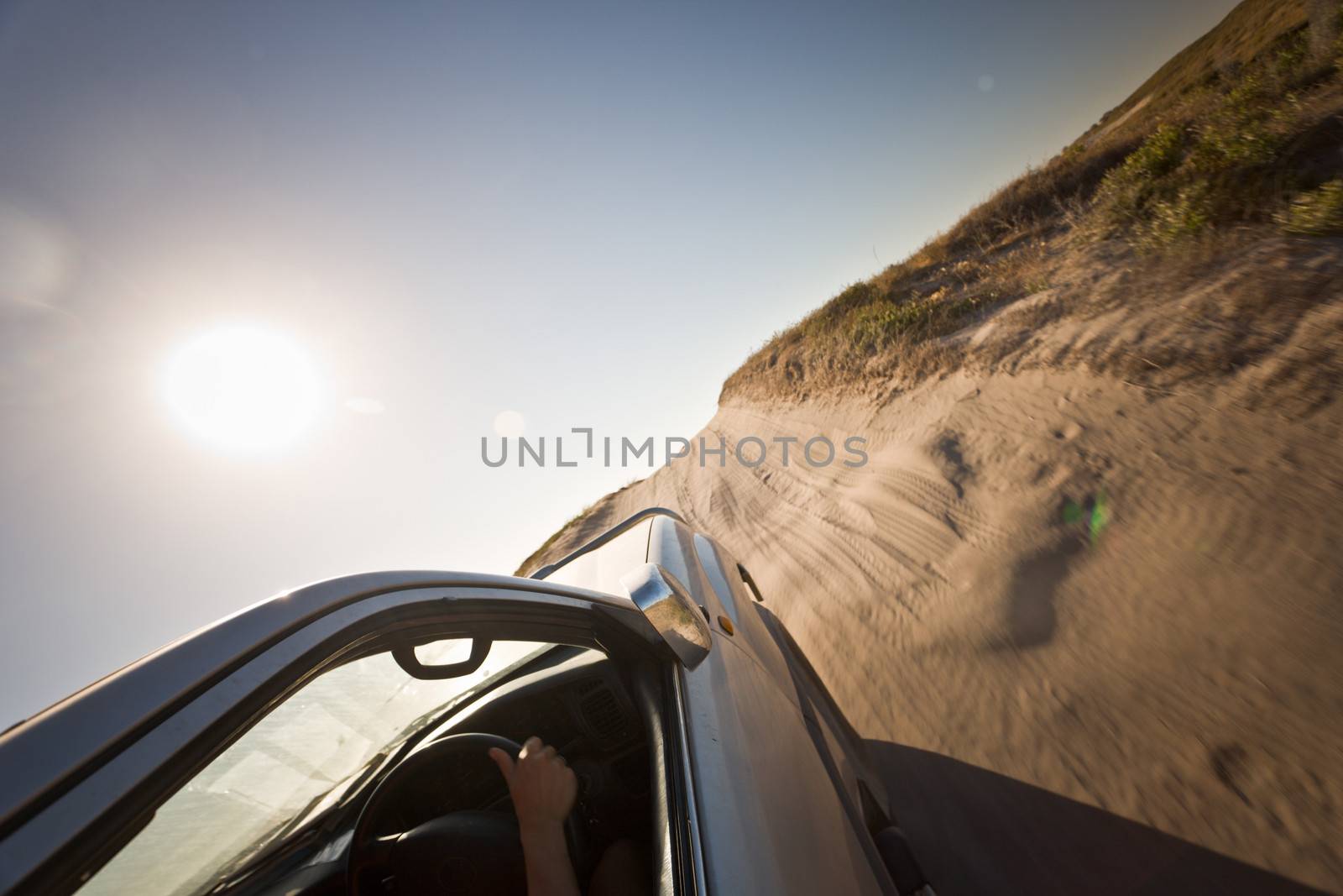 Car driving on a potholed dirt road under a searing sun across flat dry countryside