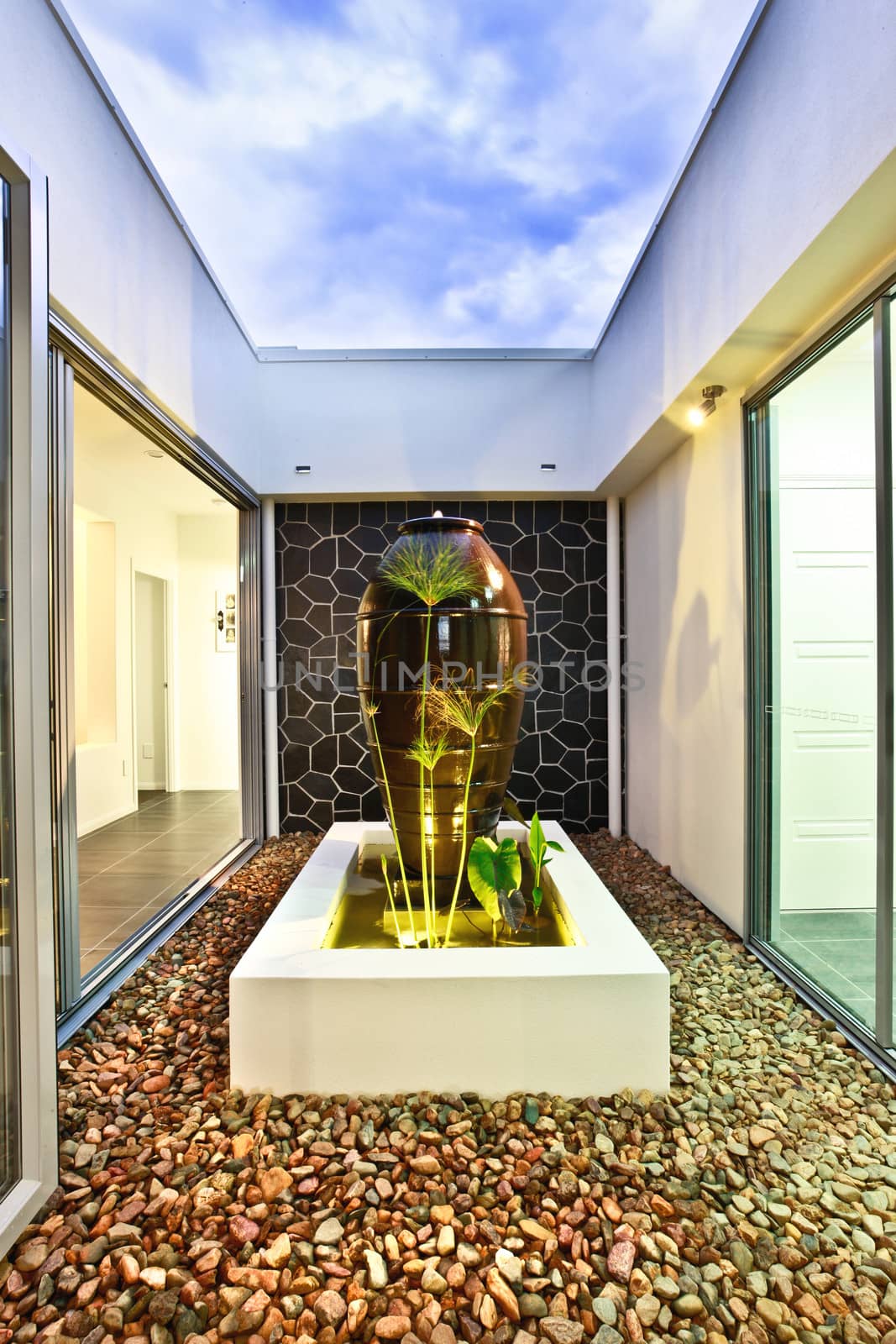 Modern sculpture in a courtyard strewn with natural pebbles running between two wings of a luxury house with large glass windows