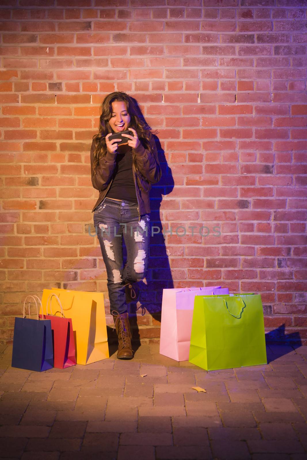 Woman with Shopping Bags Using Cell Phone Against Brick Wall by Feverpitched