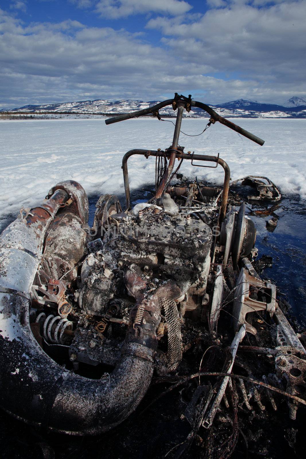 Charred remains of snowmobile burnt out in a winter motorsports mishap on frozen Lake Laberge Yukon Territory Canada