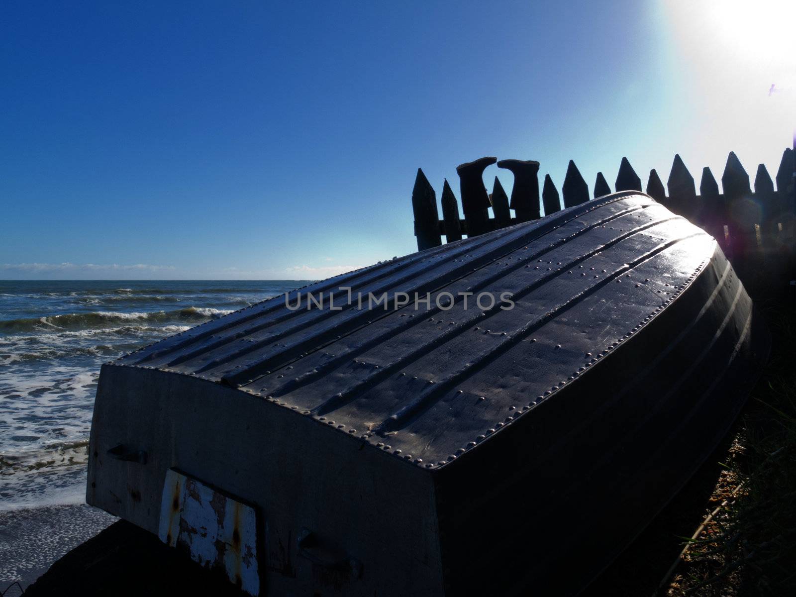 Small recreational aluminum fishing boat turned upside down on ocean coast with rubber boots drying on fence