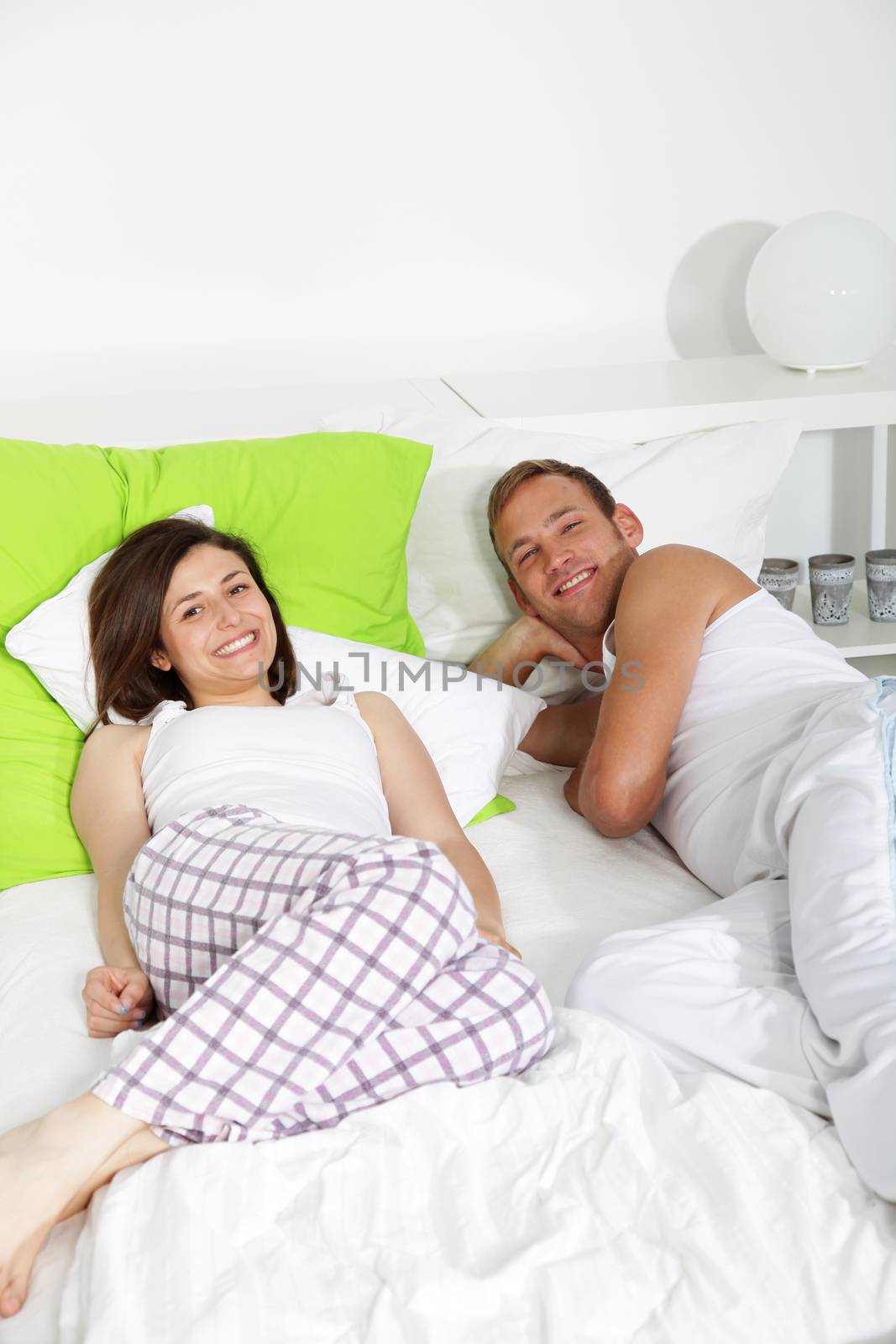 Young couple having a lazy day in bed smiling at the camera with copyspace