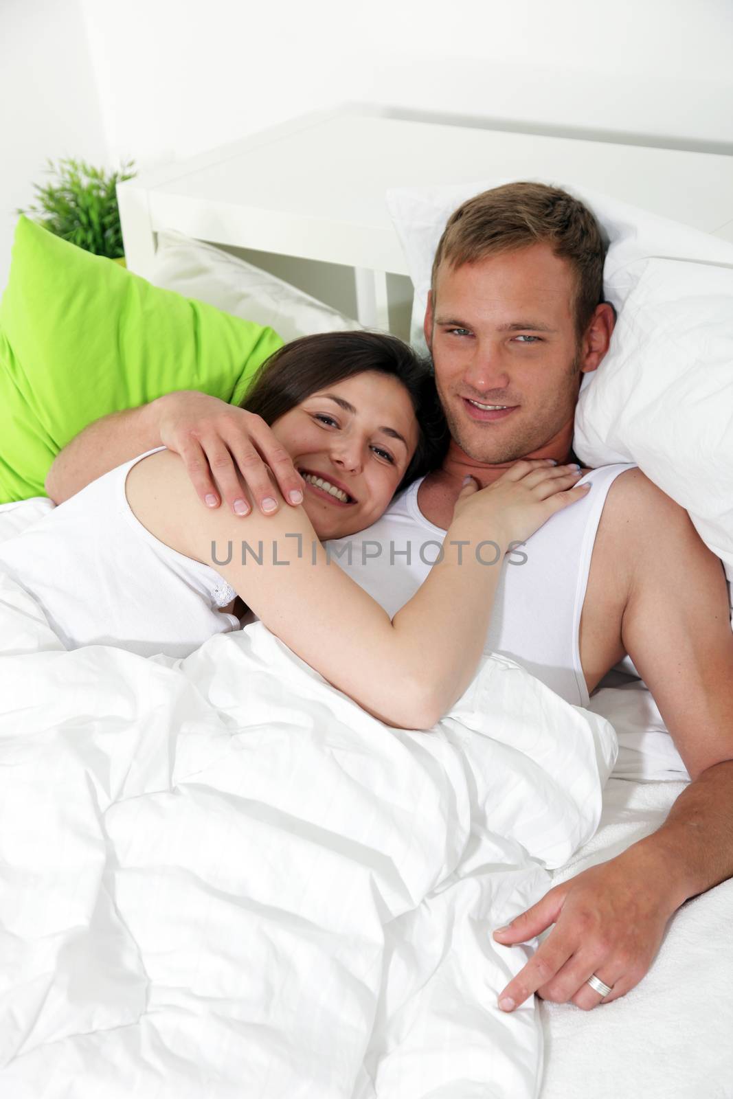 High angle view of a young loving couple resting in bed entwined in each others arms smiling in contentment