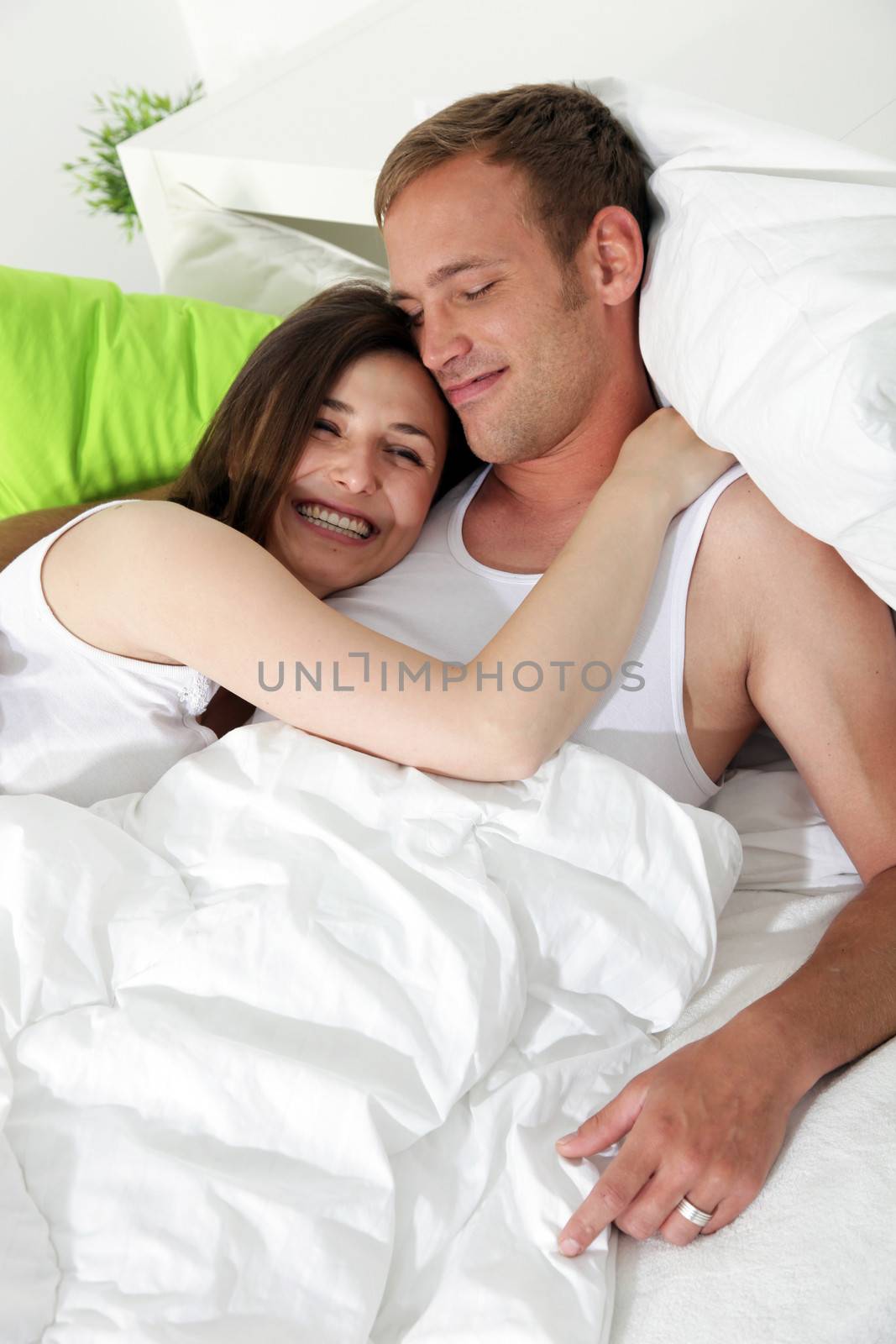 Smiling woman cuddling her husband in bed by Farina6000