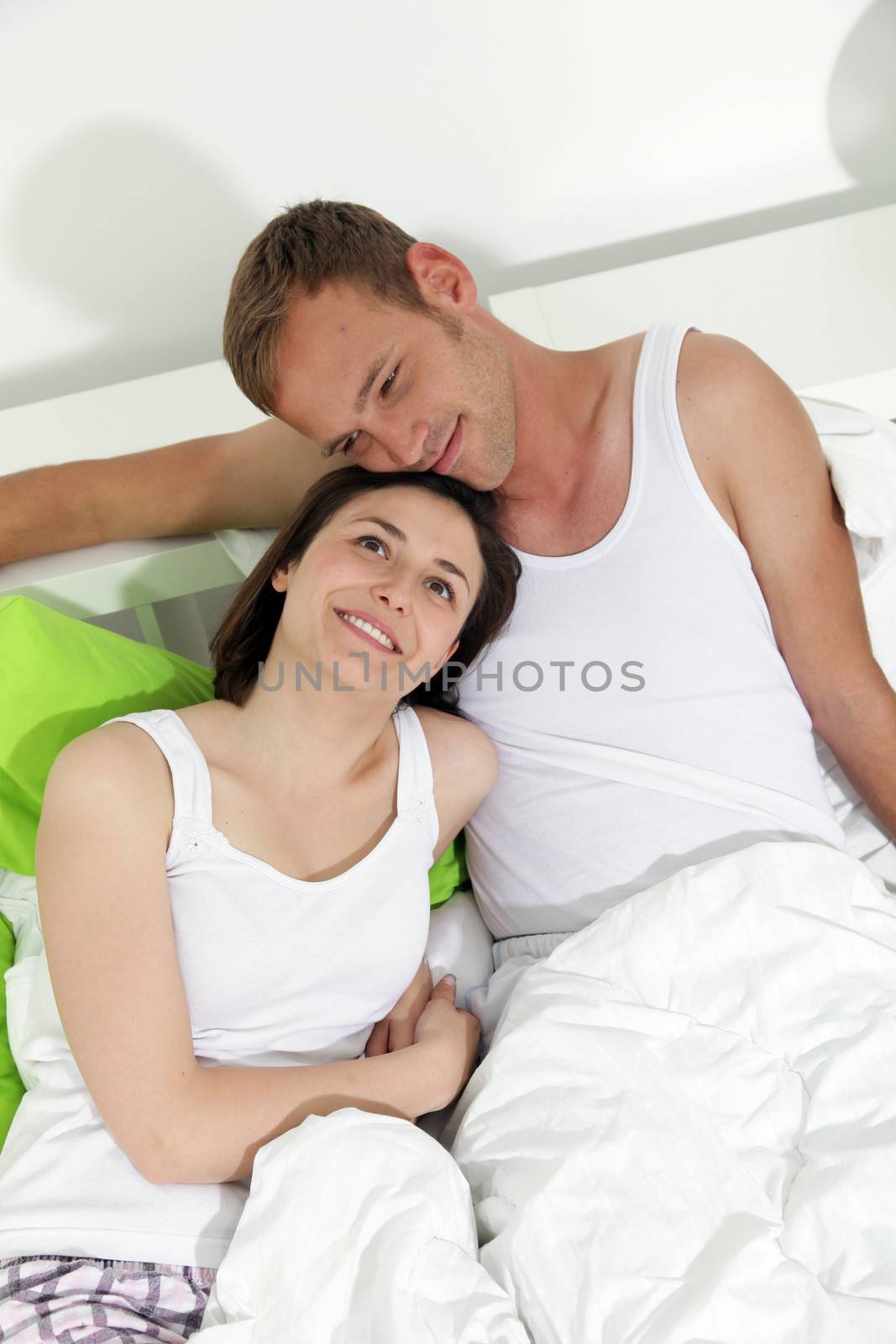 Happy young couple in bed relaxing close together on the pillows daydreaming