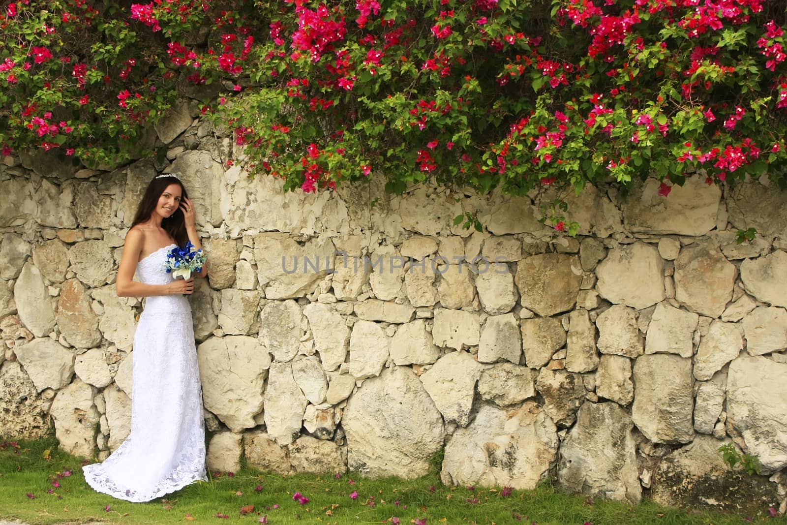 Young woman in wedding dress posing in front of the stone wall w by donya_nedomam