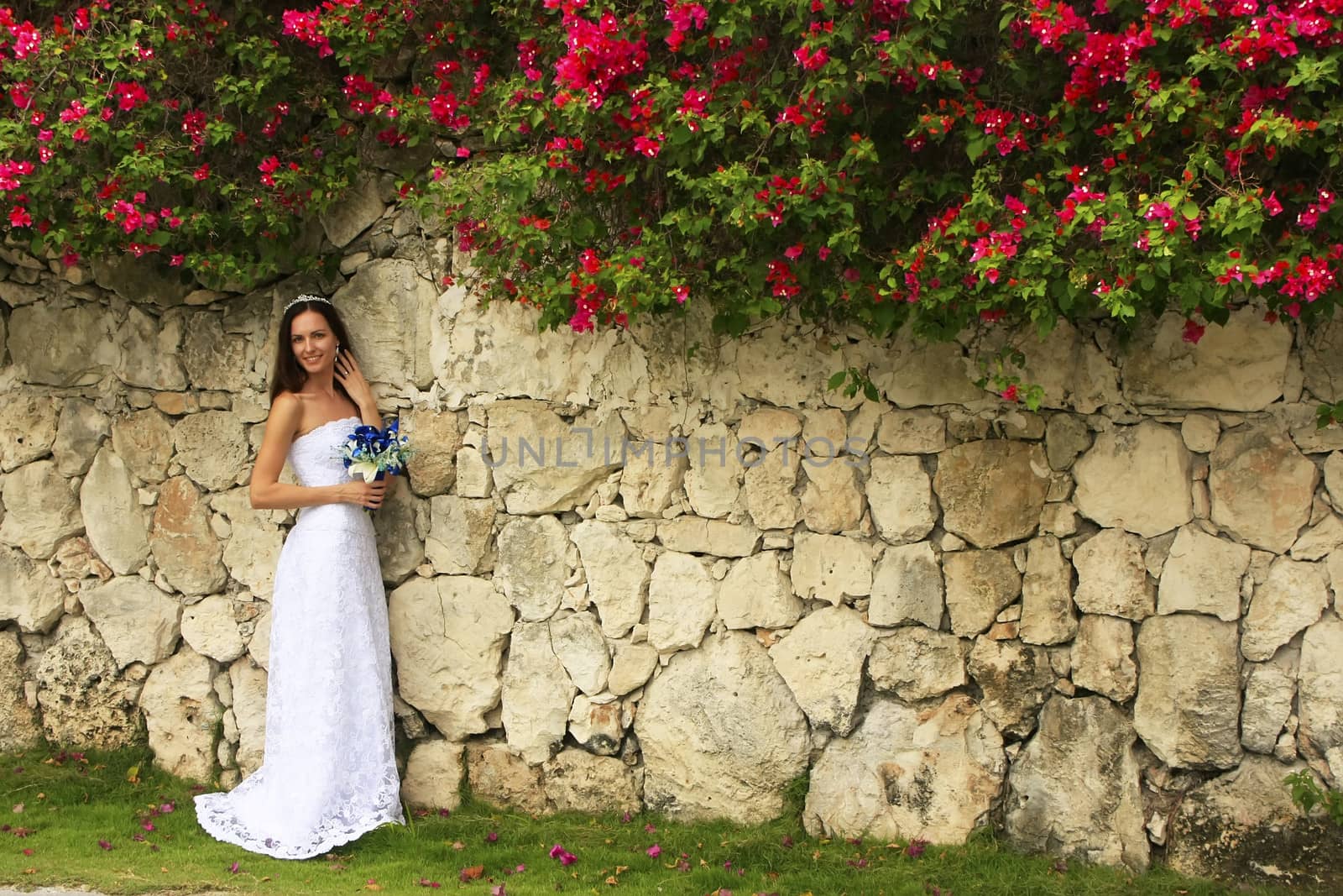 Young woman in wedding dress posing in front of the stone wall w by donya_nedomam