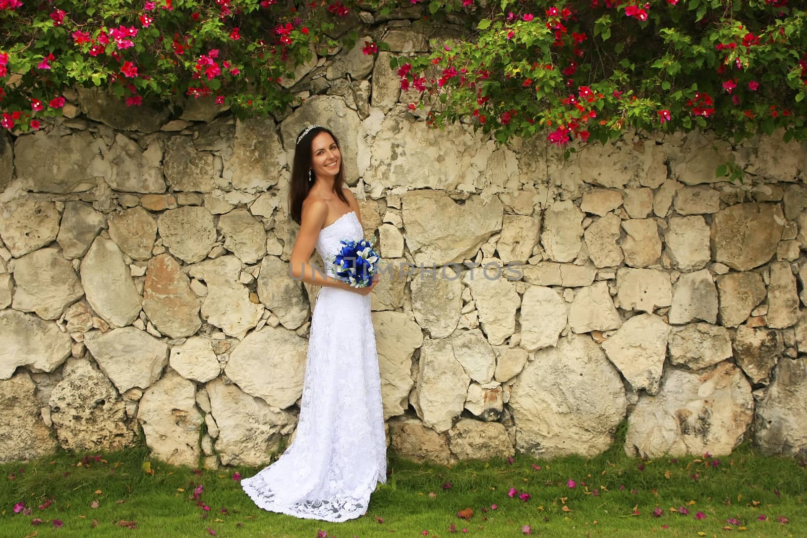 Young woman in wedding dress posing in front of the stone wall with flowers