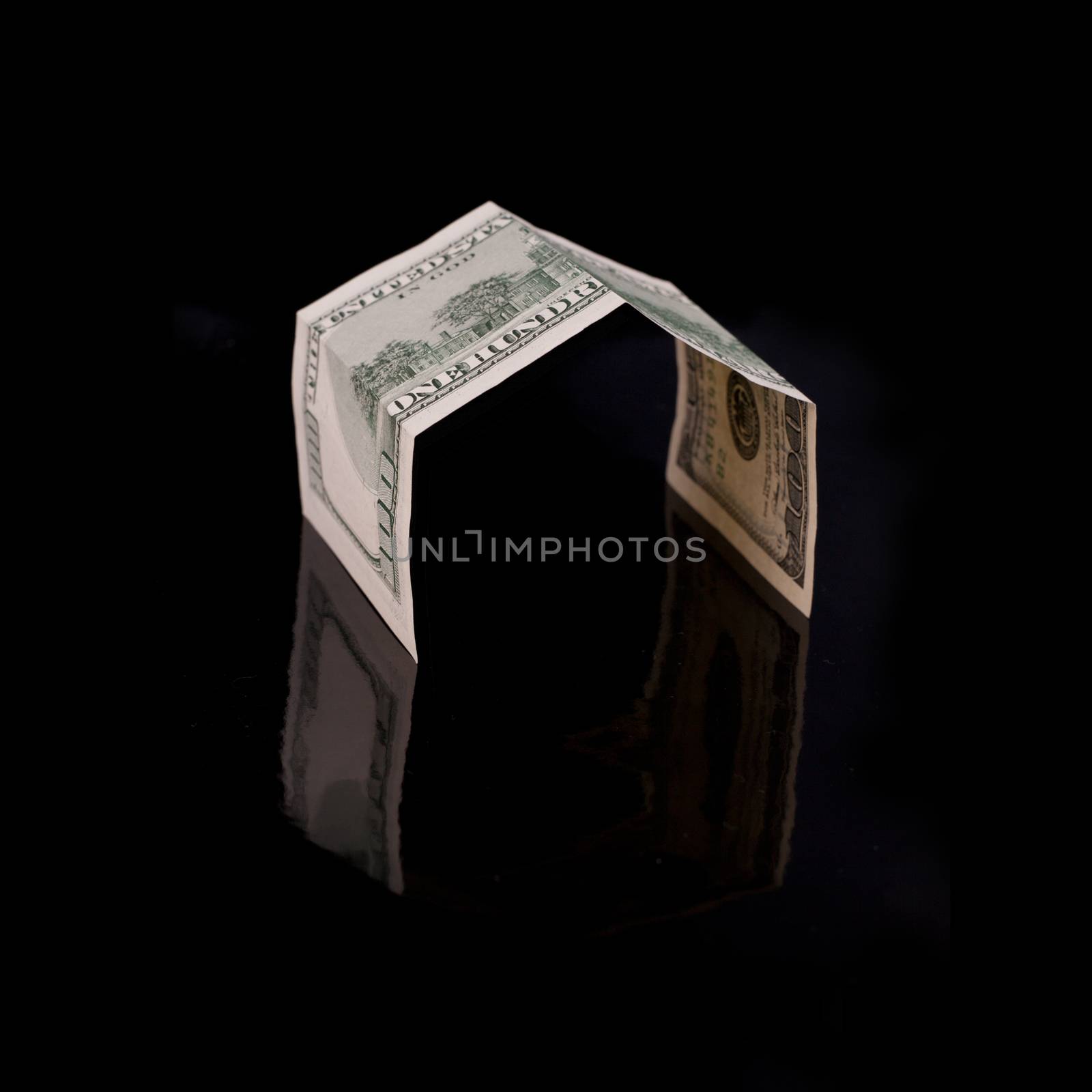 One hundred dollar bill, folded like a house on a black background with reflection