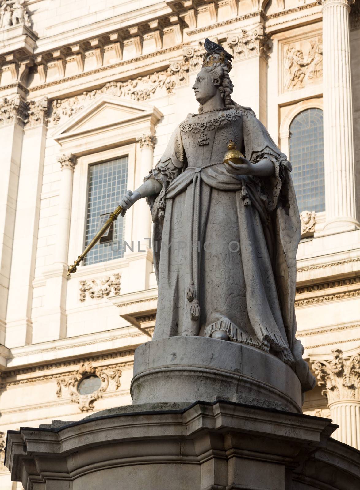 Statue of Queen Anne with bird perched on crown in St Pauls Cathedral in London England at dusk as the sun is setting low in sky.