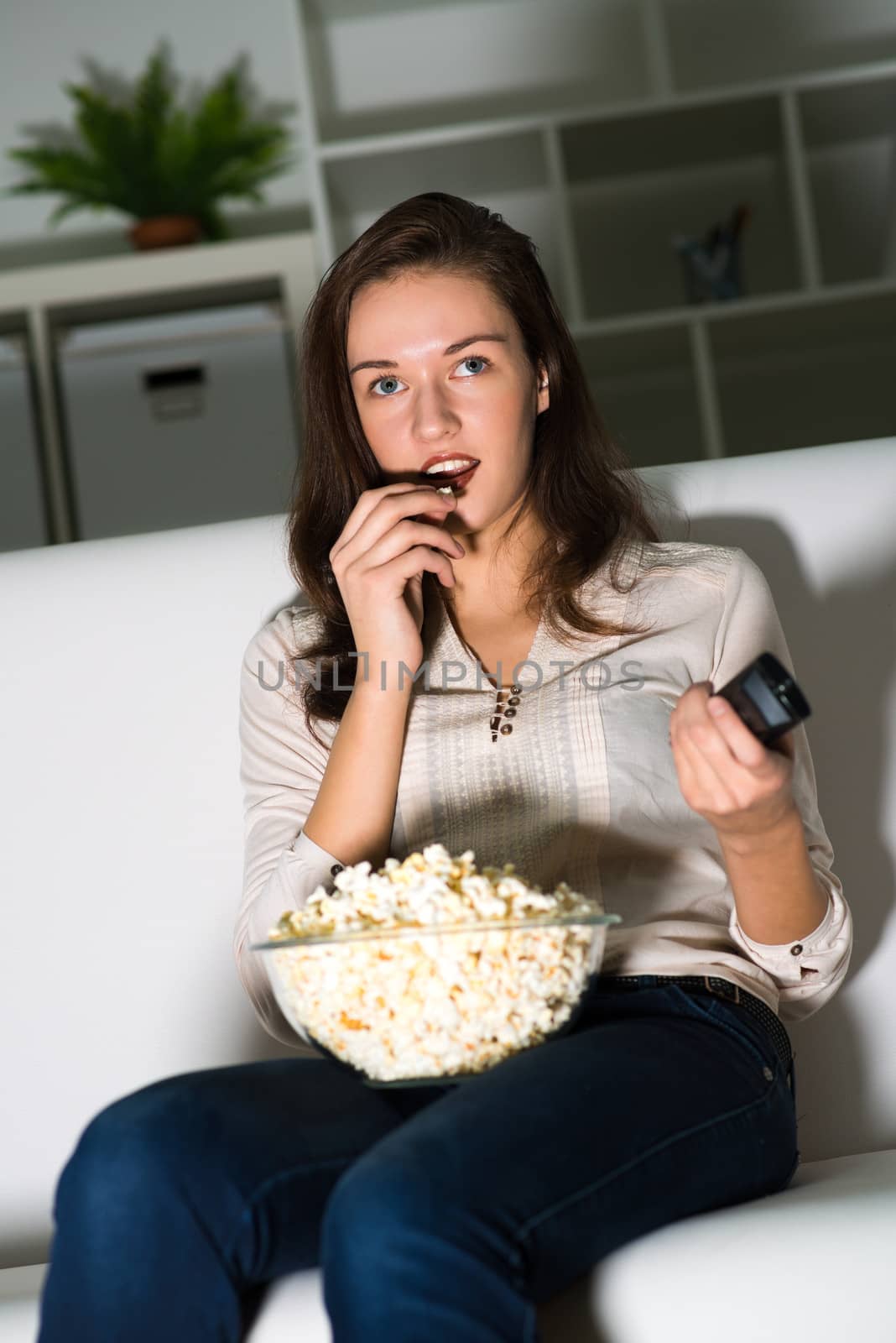 Young woman watching TV on the couch, eating popcorn