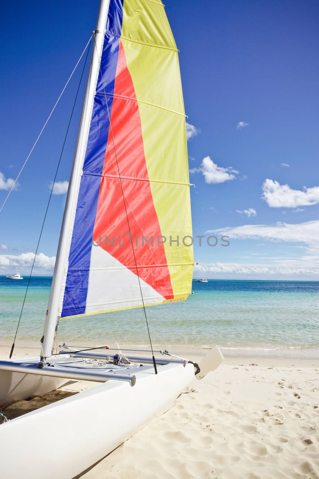 Small sailing catamaran with a colourful striped sail beached on a sandy tropical beach